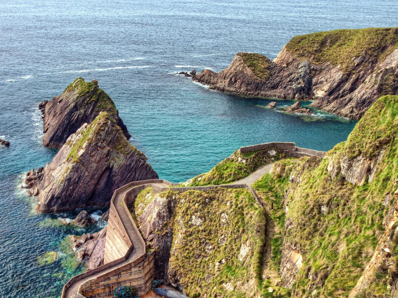 Winding pathway at Dunquin Pier and unique rock formations over a calm sea at Dingle Peninsula, a piece on the best places to visit in Ireland
