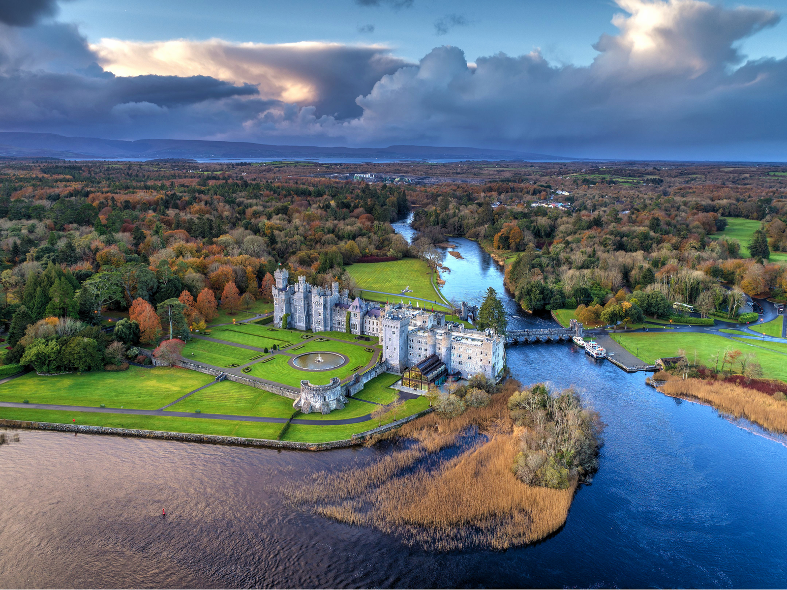 Aerial view on the enormous Ashford Castle, a piece on the best places to visit in Ireland, erected beside a large river and dense forest