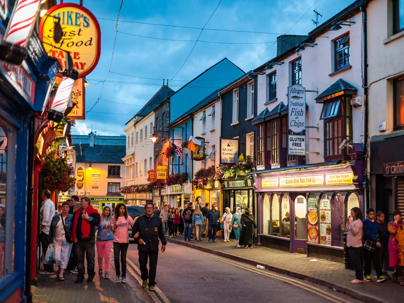 Busy dusk at Killarney town, one of the best places to visit in Ireland, where people are seen waking along sidewalks beside pubs and restaurants