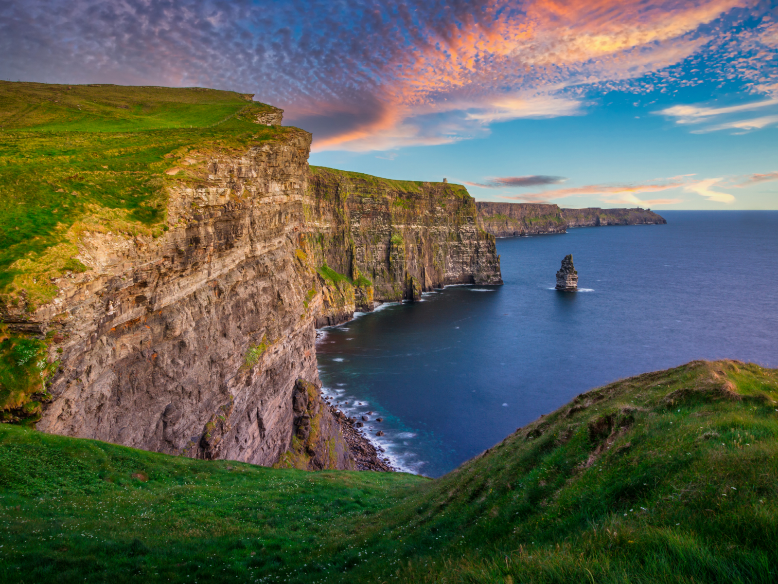 A scenic sunset over the towering Cliffs of Moher, one of the best places to visit in Ireland, layer of green pasture at the top