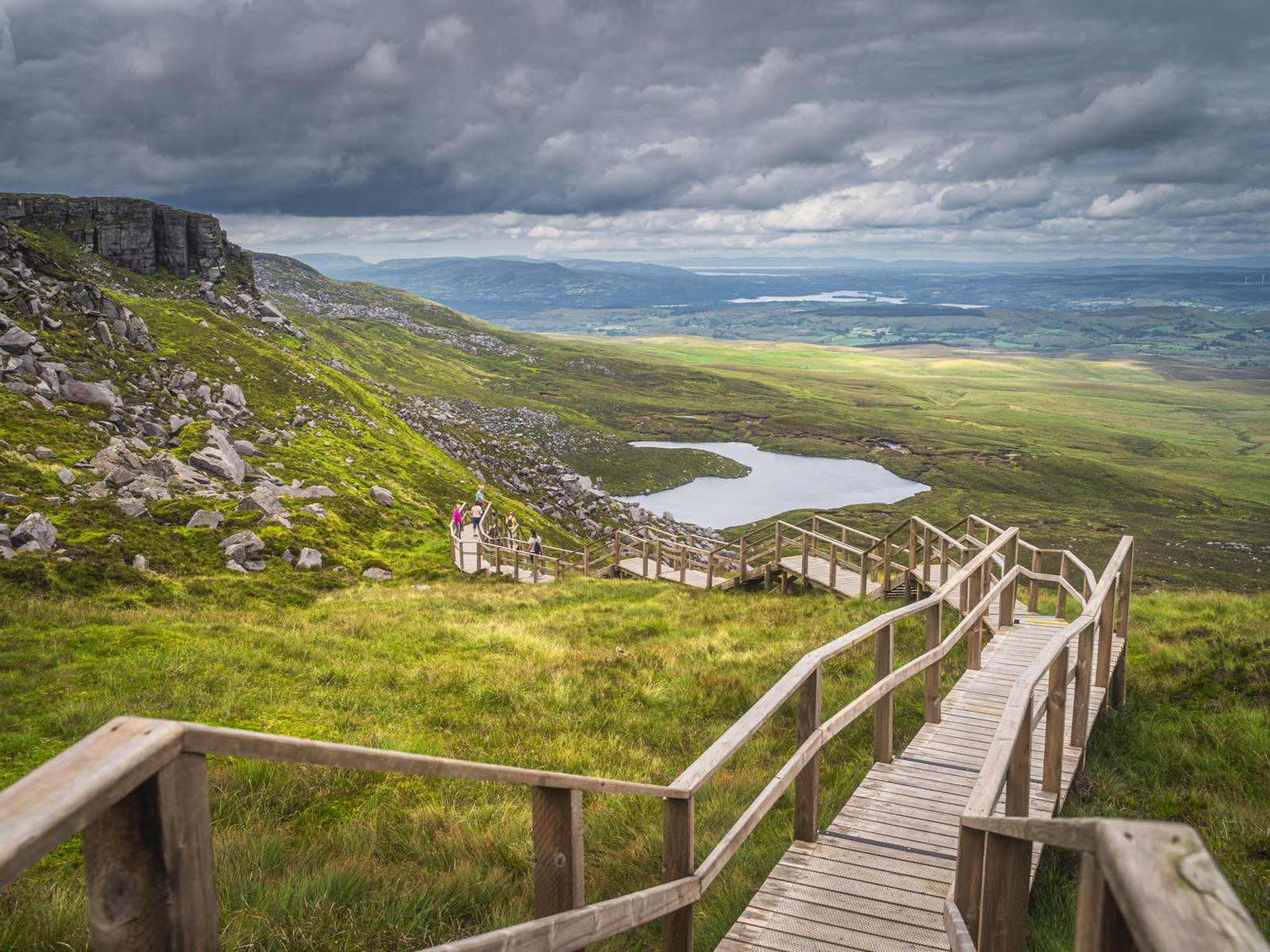 Visitors climbing down a long sloppy boardwalk at Cuilcagh Mountain Park, one of the best places to visit in Ireland, on an overcast day