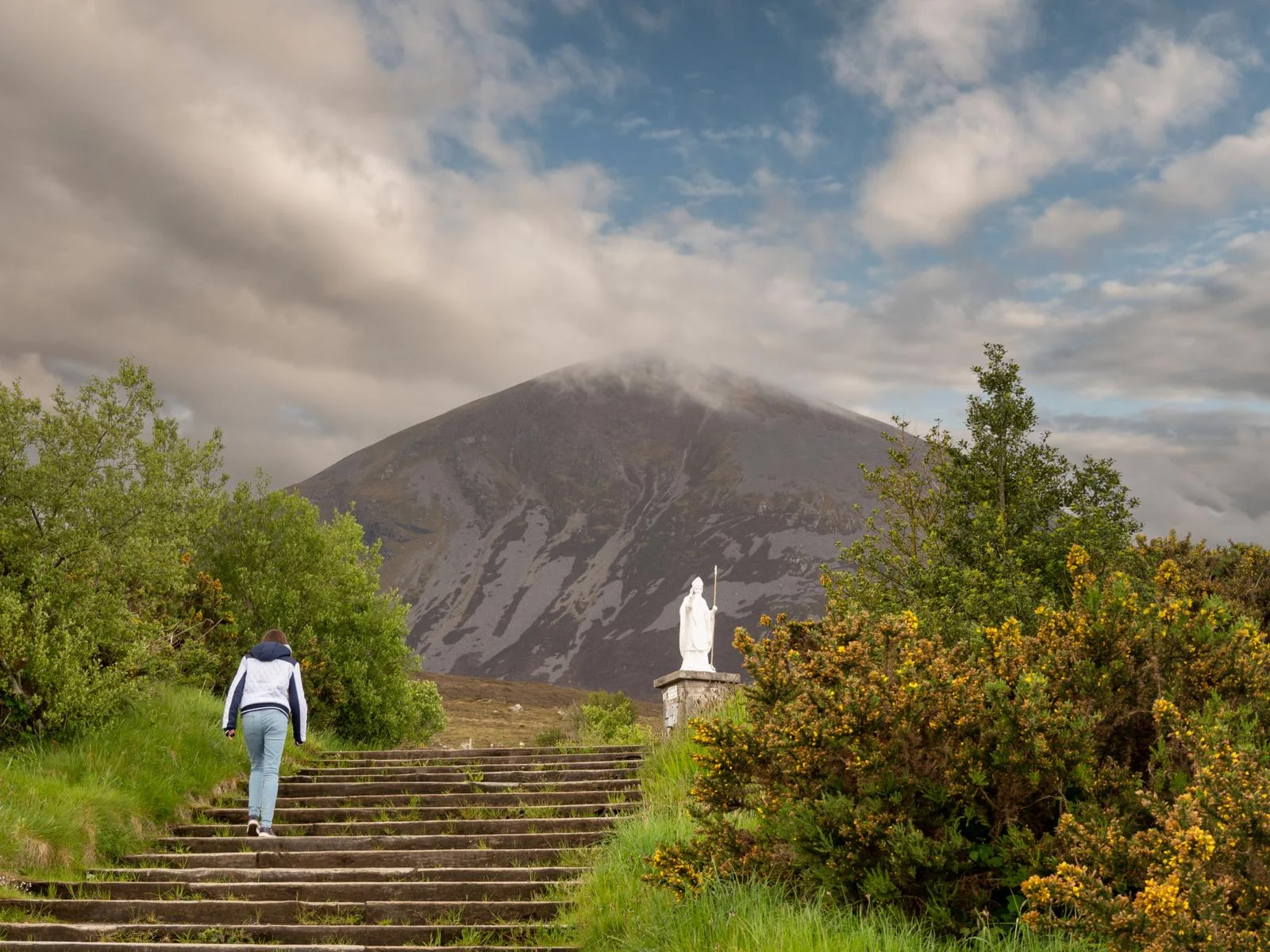 A young woman climbing up stairs to cloudy peak Croagh Patrick, one of the best places to visit in Ireland