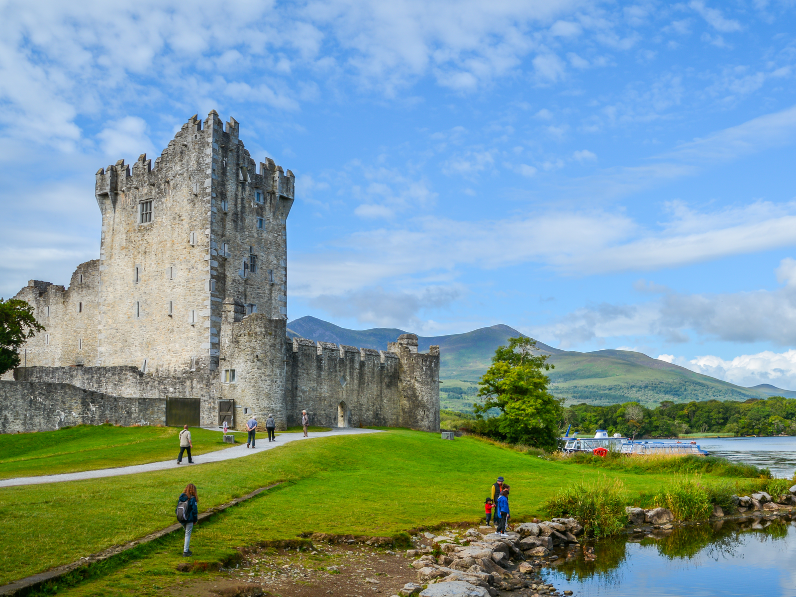 Tourists wandering off the green yard of Ross Castle at Killarney, one of the best places to visit in Ireland