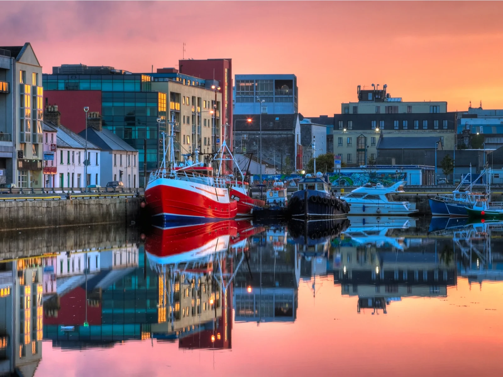 Young sunrise over the Galway Dock with fishing boats reflected on the mirror-like still water, a piece on the best places to visit in Ireland