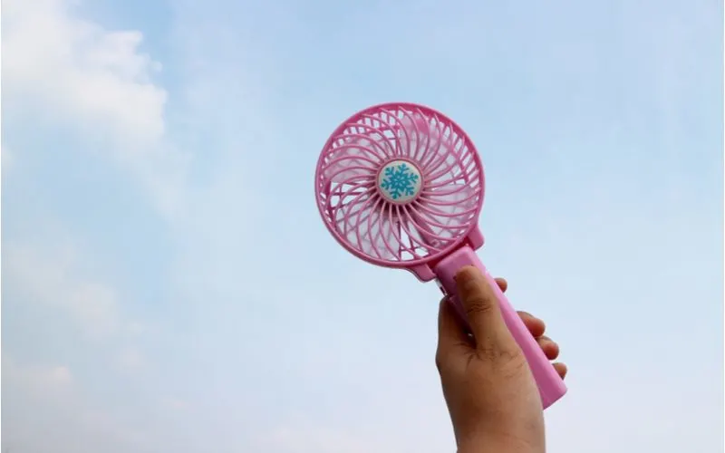 Best portable fan being held by a masculine hand against a sky