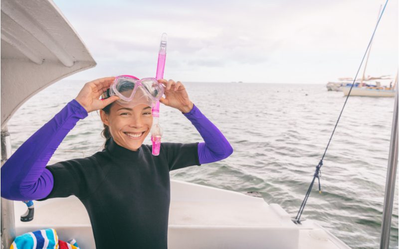 Woman wearing the best snorkeling gear with a mask and a snorkel and a wetsuit on a boat smiling