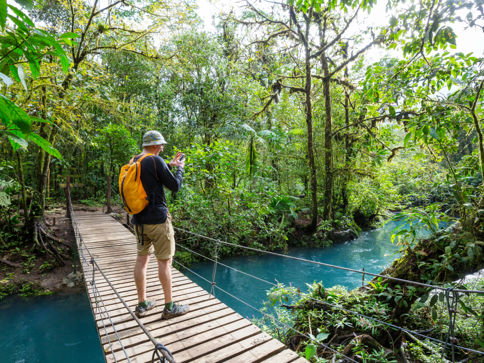 Guy hiking in the tropical green jungle with teal water below him in La Fortuna, one of our picks for where to stay in Costa Rica