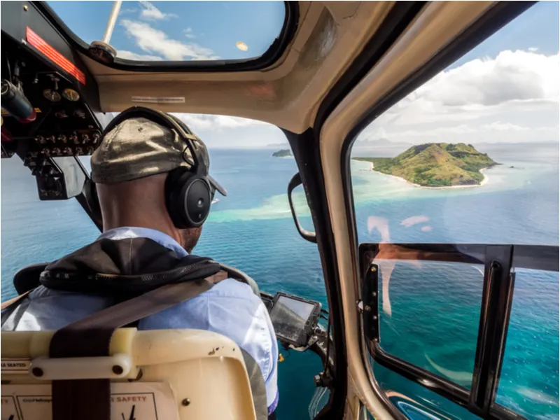 Over-the-shoulder shot of a blue hawaiian helicopter over an island, one of the best things to do in Hawaii