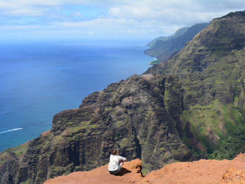 Woman sitting on the edge of one of the best hikes in Kauai, the Nu’alolo Trail