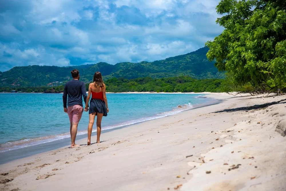 Attractive and tall young couple holding hands and walking down the beach in Costa Rica