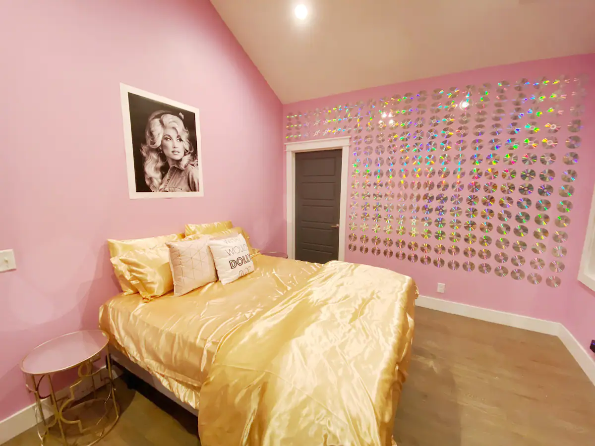 CDs perfectly lined on the pink wall and a bed with golden bed sheets, pillows, and blankets at Nashville’s Original Bachelorette House, one of the best bachelorette Airbnbs