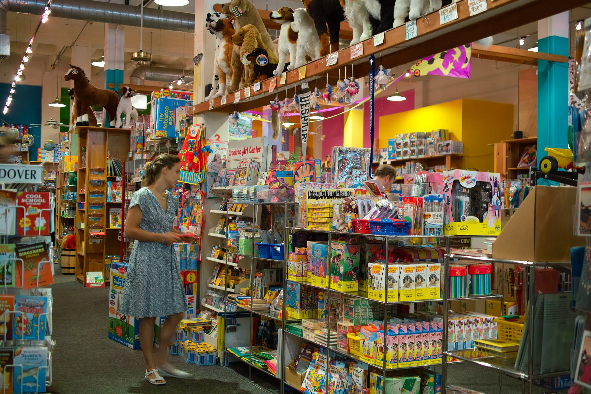 A woman wearing dress choosing from various toys displayed in shelves at Finnegan’s Toys & Gifts in Portland, one of the best toy stores in America