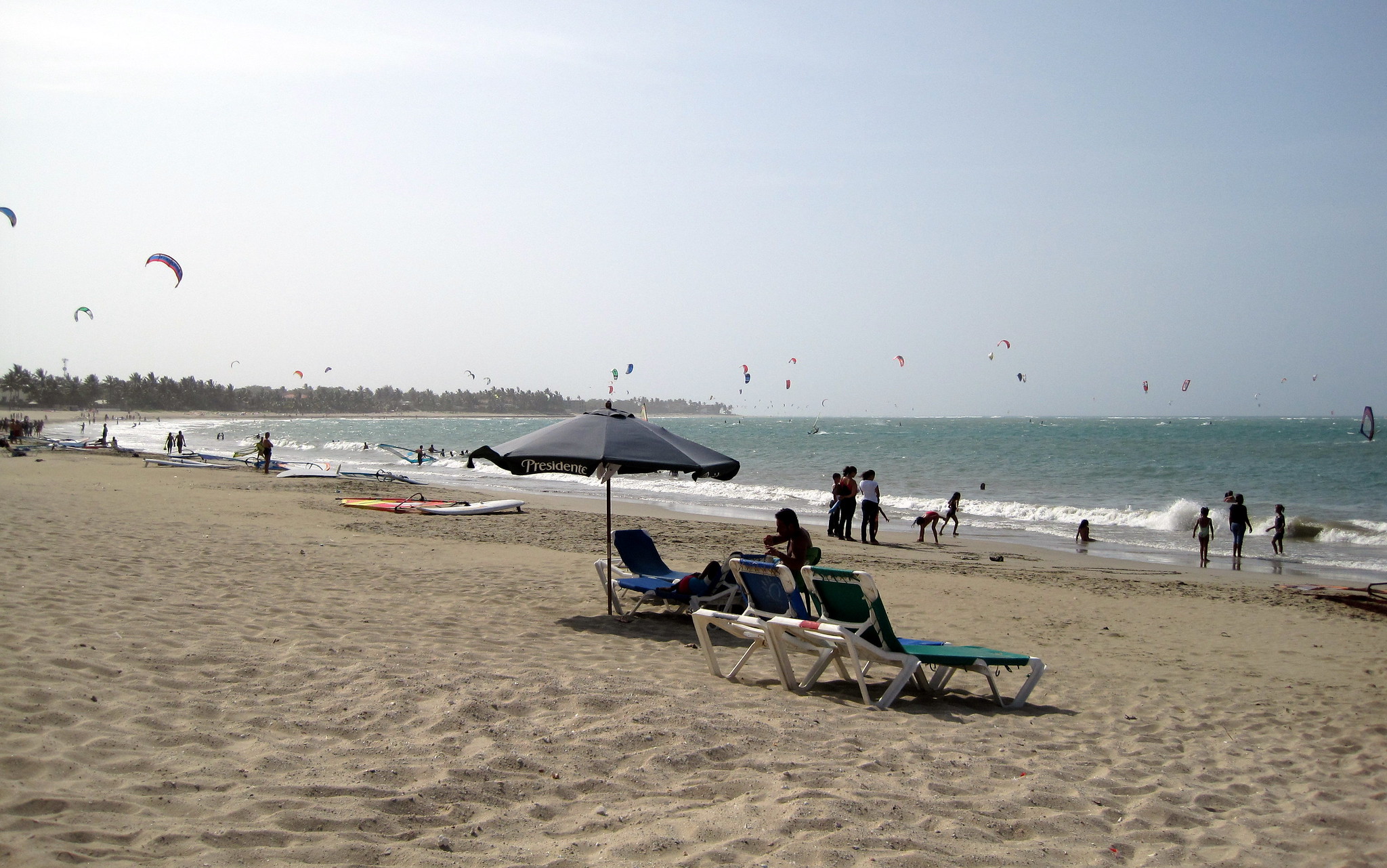 Tourist enjoying a hot sunny day at Playa Cabarete in Cabarete, one of the best beaches in the Dominican Republic, with a number of kitesurfers offshore