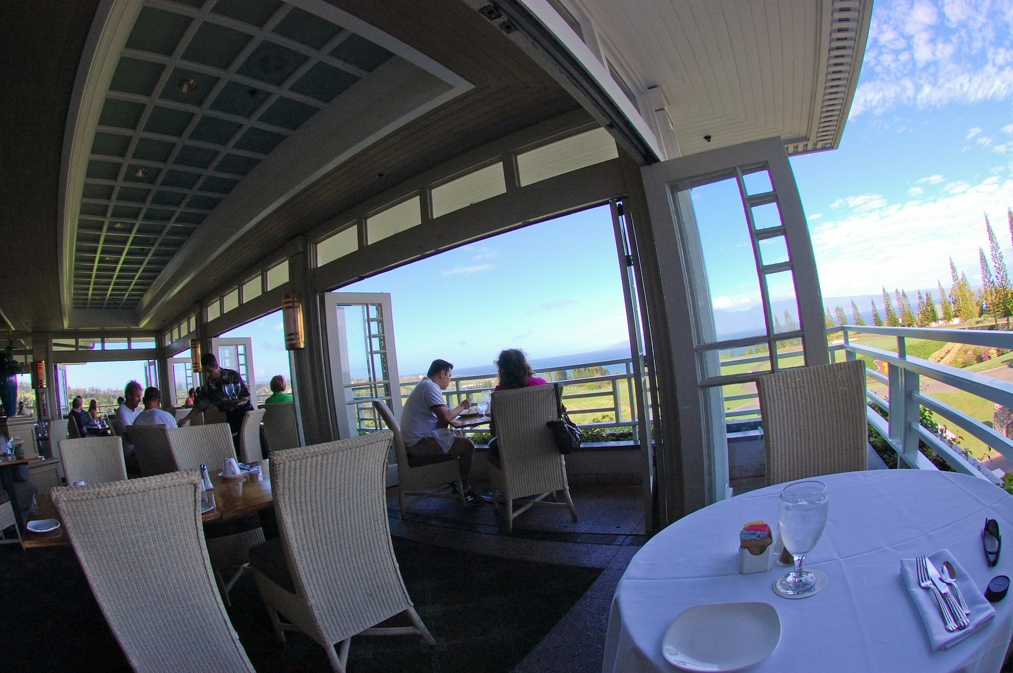 Fish-eye view inside The Plantation House, labeled as one of the best restaurants in Maui, Hawaii, where diners enjoy their meals and a crew serving drinks with a vast landscape in background