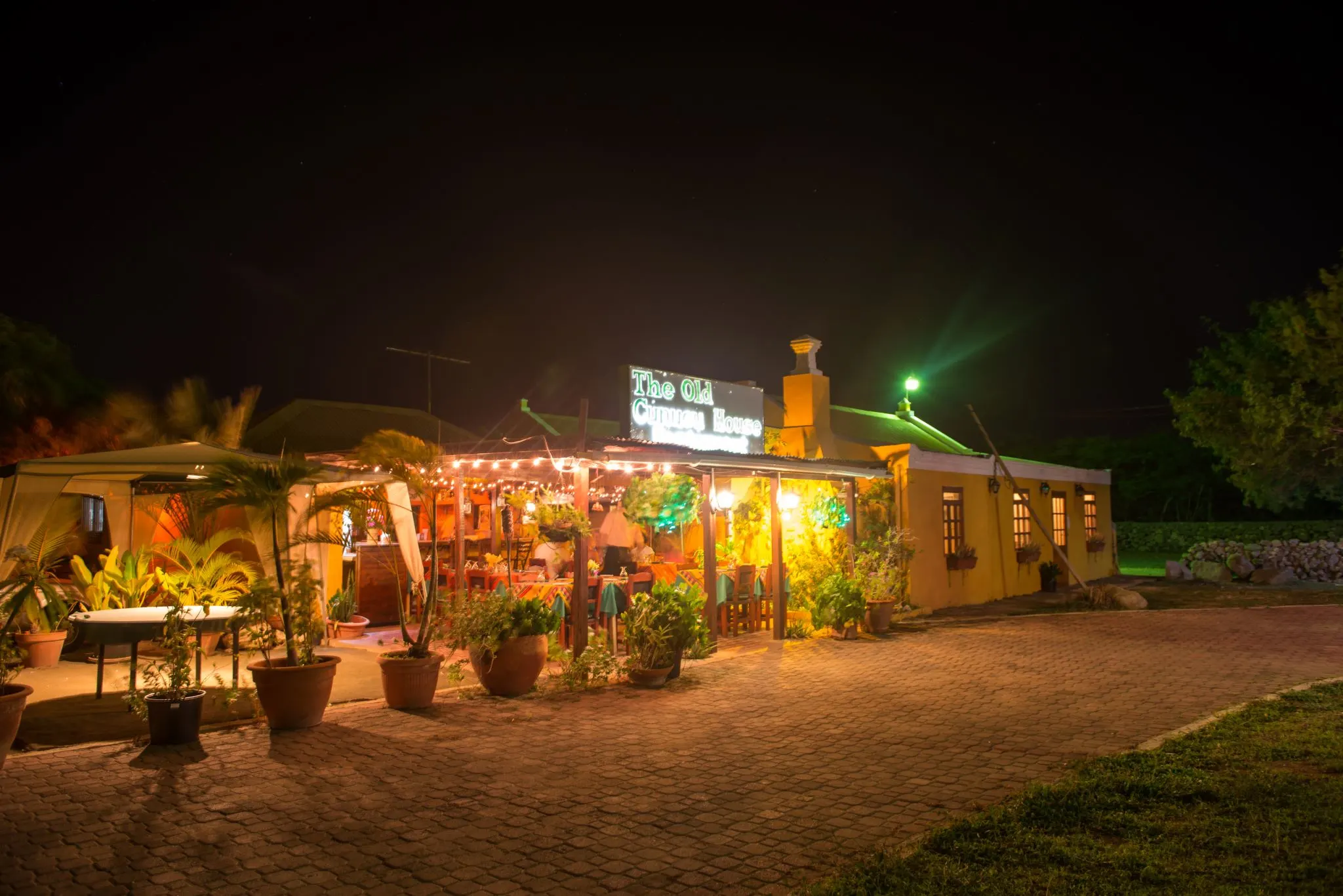 The bright lights of The Old Cunucu House Aruba at night, one of the best restaurants in Aruba, with bricks and potted plants on the front