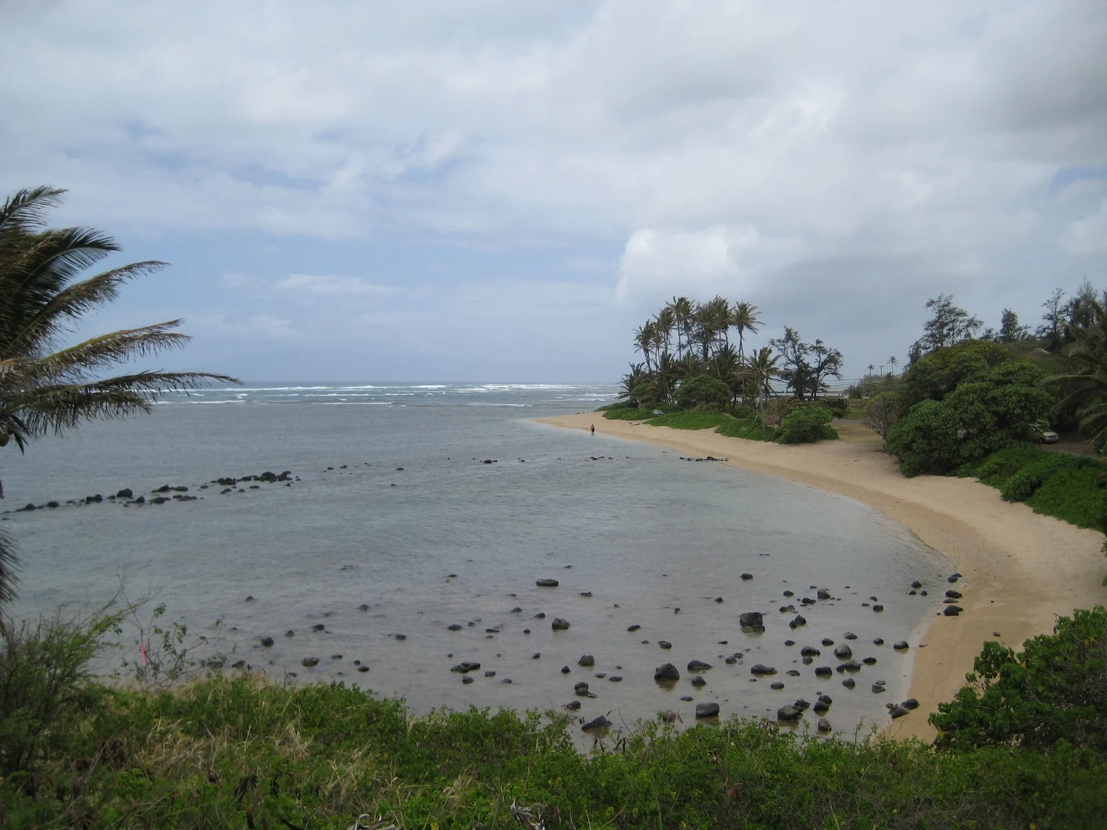 A person walking on the shallow and rocky beach line of Kumimi Beach, also known as Murphy’s Beach, one of the best snorkeling spots in Hawaii