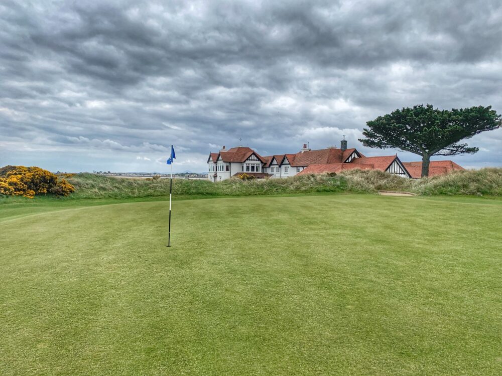 The clubhouse of Portmarnock Golf Club, a piece on the best golf courses in Ireland, at corner of the wide green golf course with a small blue flag