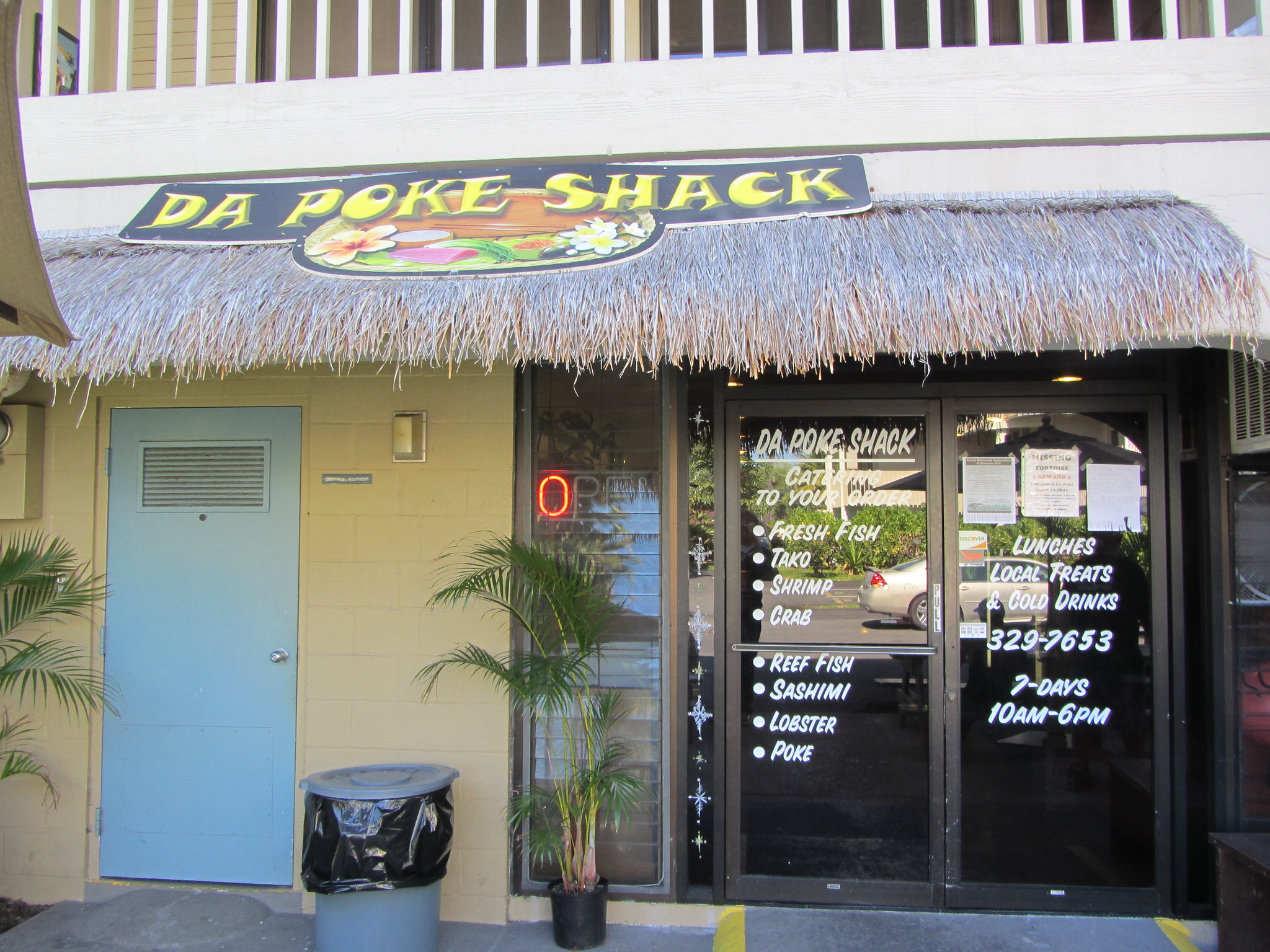 The classic native-themed storefront of Da Poke Shack, listed as one of the best restaurants in Kona, Hawaii, where featured dishes printed on tented glass door