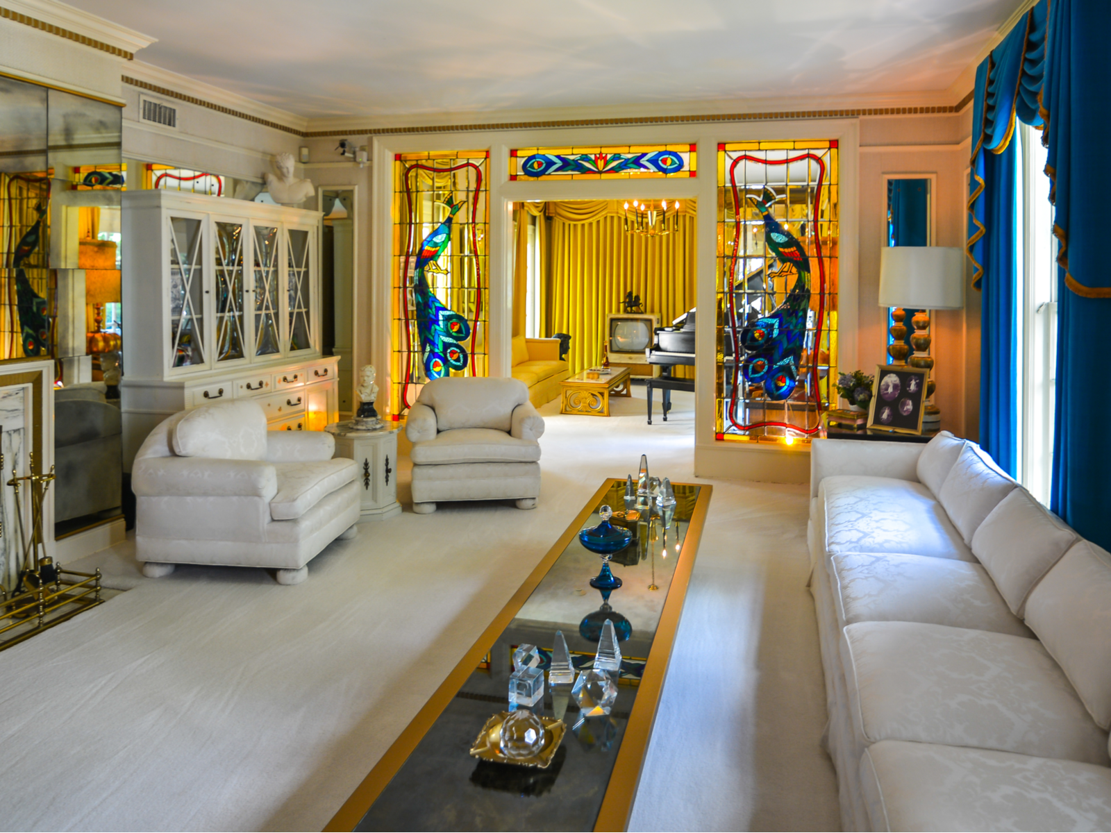 Living room of the famed Graceland Mansion, one of the best places to visit in Tennessee, which was once an abode of Elvis Presley with white and gold furnitures, white carpet, and stained glass depicting a peacock