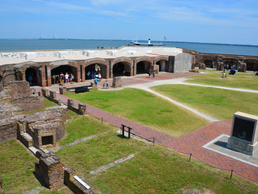Aerial view on Fort Sumter National Monument's green open field, known as one of the best South Carolina attractions, where people are gathered at an old structure for a historical exhibit