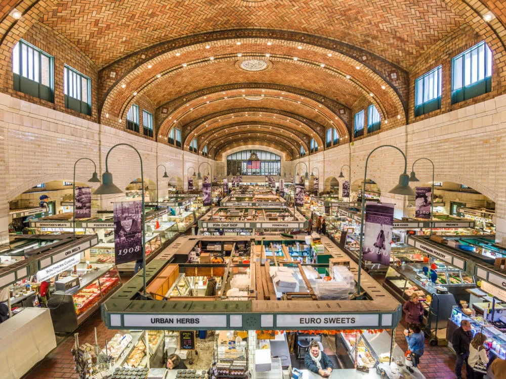 viewing the high ceiling layered with bricks at West Side Market with lively stalls of various goods and some customers is one of the best things to do in Ohio