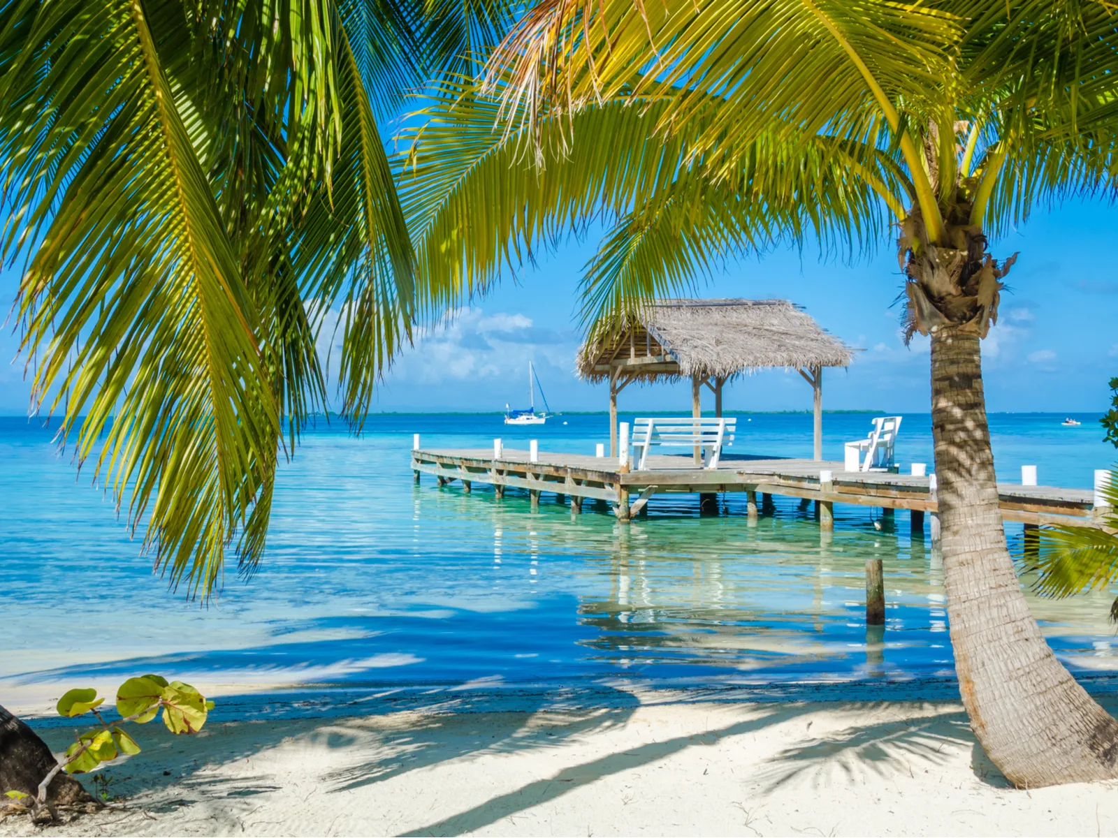 Belize Caye pictured during the cheapest time to visit with a pier jutting into gorgeous teal water