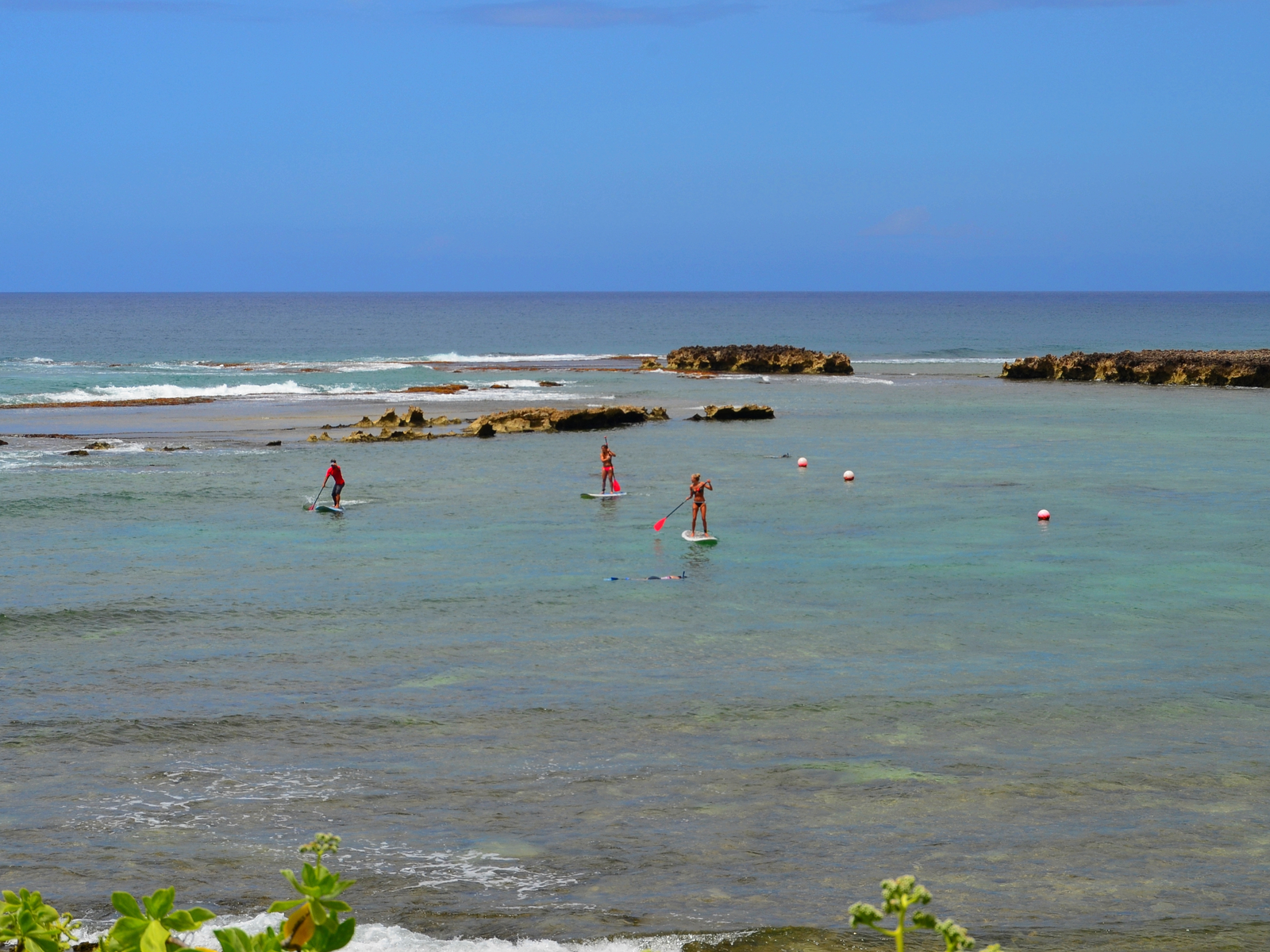 Three people paddle boarding and two snorkeling at the rocky Kuilima Cove, one of the best snorkeling spots in Hawaii