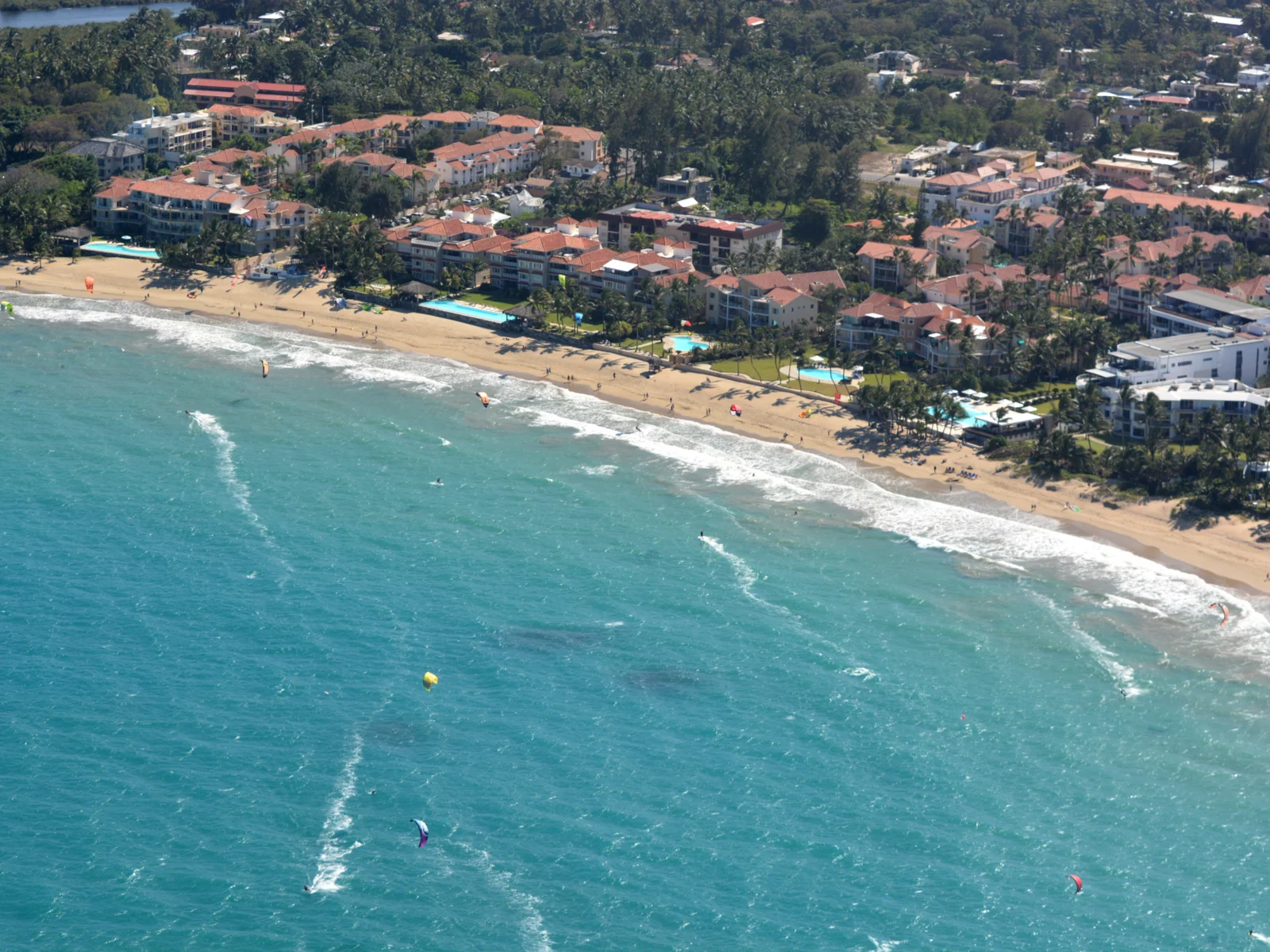 Aerial view of kite surfers riding the waves ad wind at Kite Beach in Cabarete, one of the best beaches in the Dominican Republic, with some people on the beach and hotels offshore 