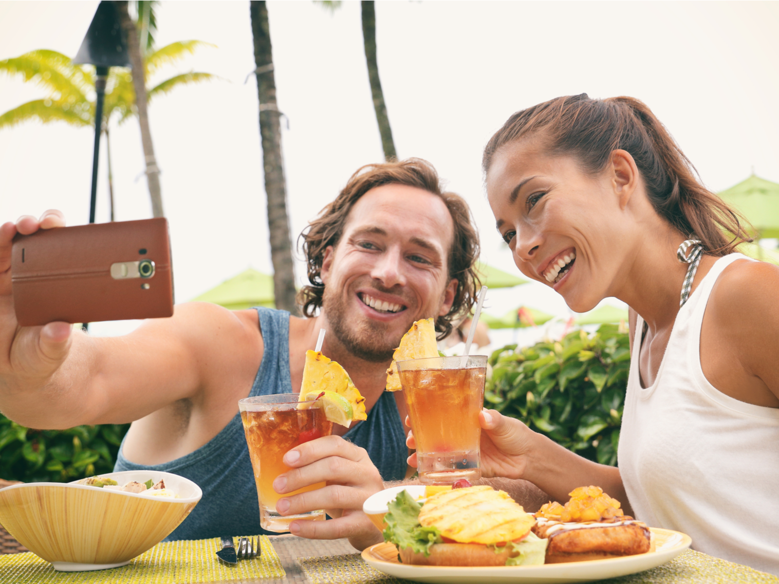 A happy couple taking a selfie before taking a sip on the ice-cold tropical drink at one of the best restaurants in Maui, Hawaii