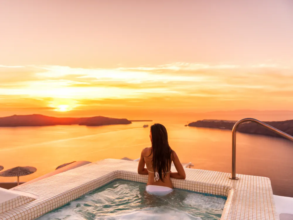 Happy women in a white swimsuit looking out over the ocean from a hot tub at one of the best hotels in Santorini