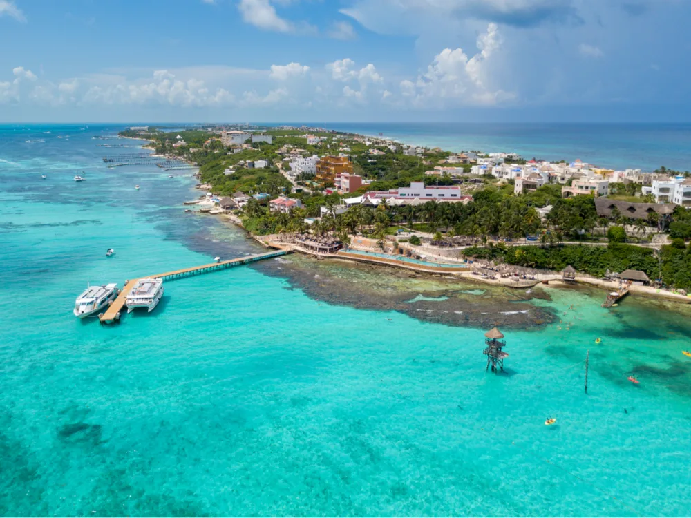 Arial view of Isla Mujeres, one of the best things to do in Cancun, with two boats docked on a small boardwalk and the populated area of the island