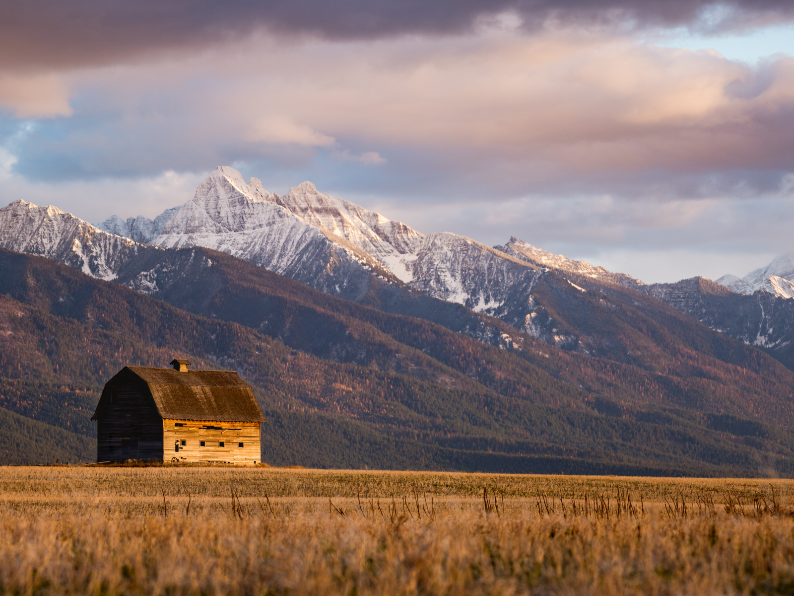 A lonely old barn at a valley bellow snowy peak mountain ridges in Pablo, one of the best things to do in Montana