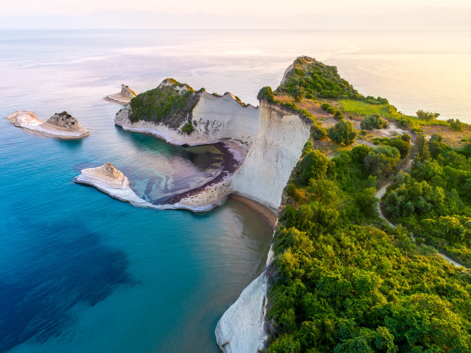 Aerial view on the white cliffs at Cape Drastis in the island of Corfu as one of the best islands in Greece to visit, with lush greeneries at the top and calm clear sea at the bottom