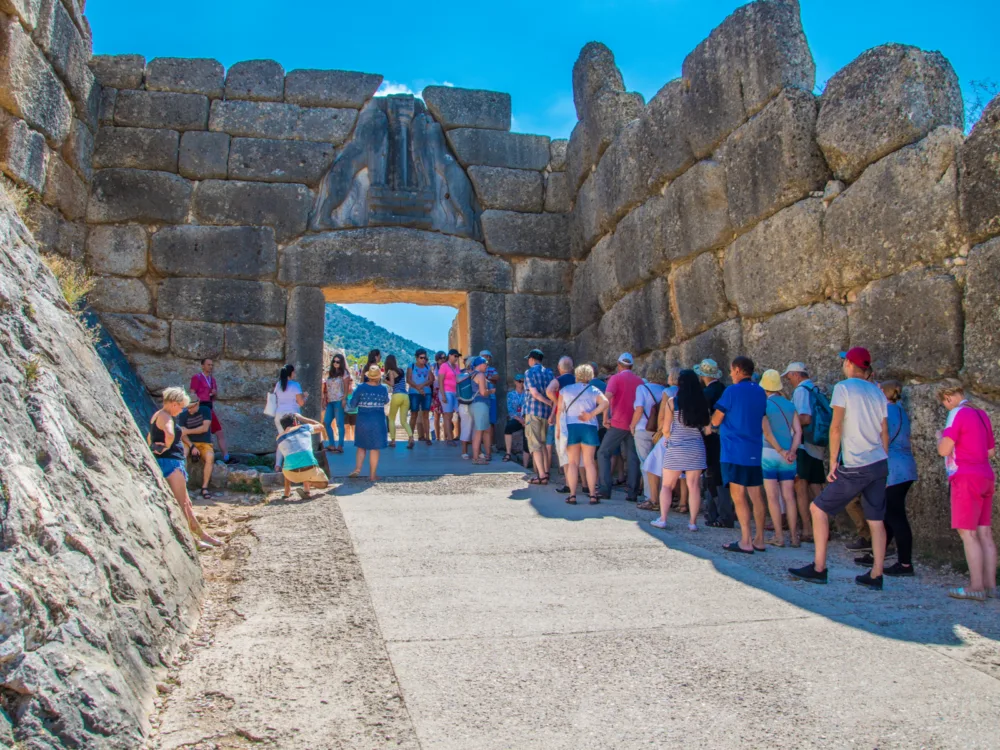 Tourists queuing while taking shade on the shadow casted by an old wall at Lion's gate main entrance of the Citadel of Mycenae, one of the best places to visit in Greece