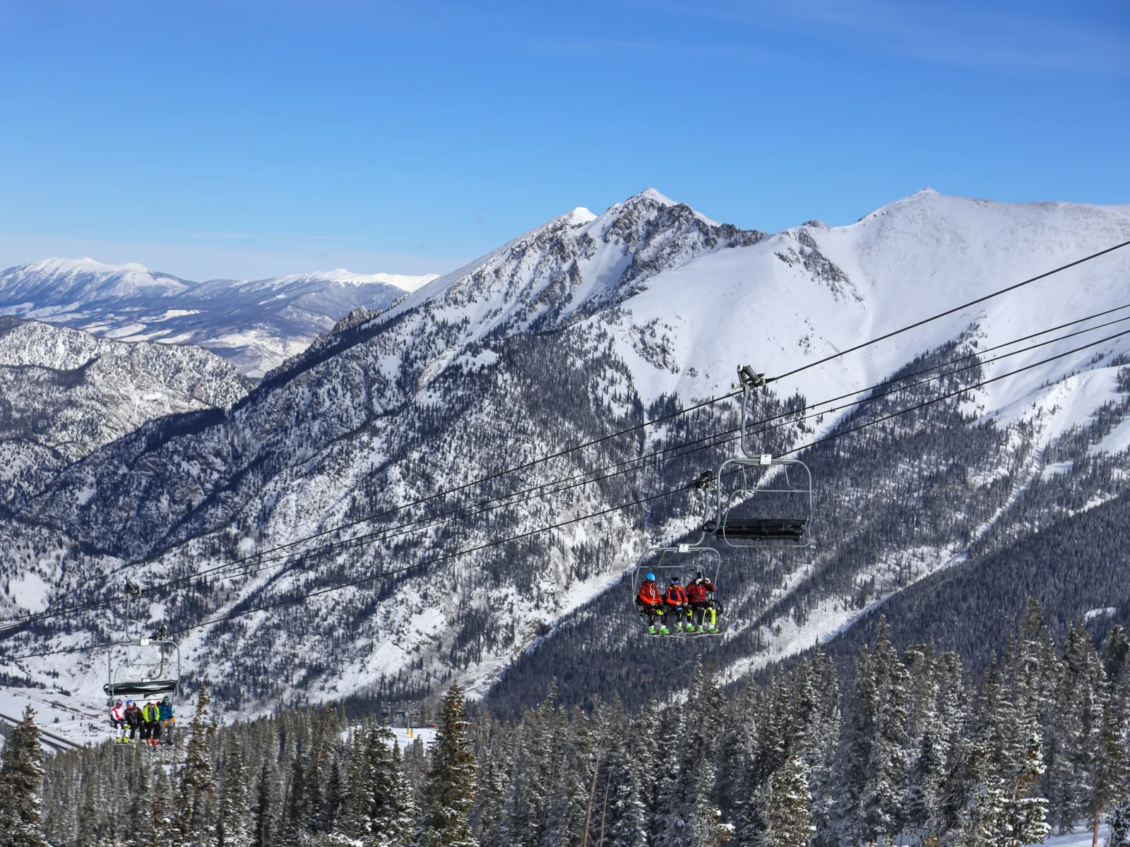 Two groups of skiers riding up a chairlift during a clear winter sky in Copper Mountain Ski Resort, one of the best ski resorts near Denver