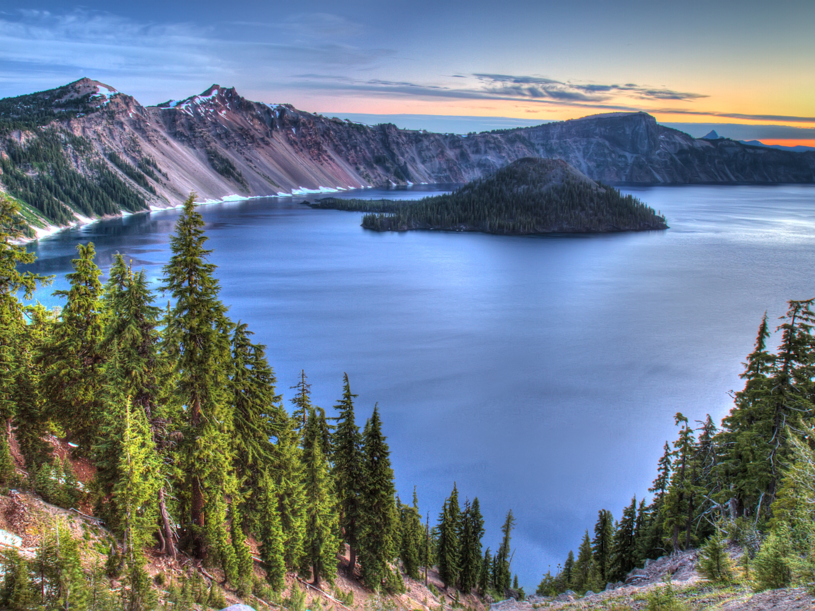 Sunrise over Crater Lake, one of the best places to visit in Oregon, with a gorgeous treeline and lake view