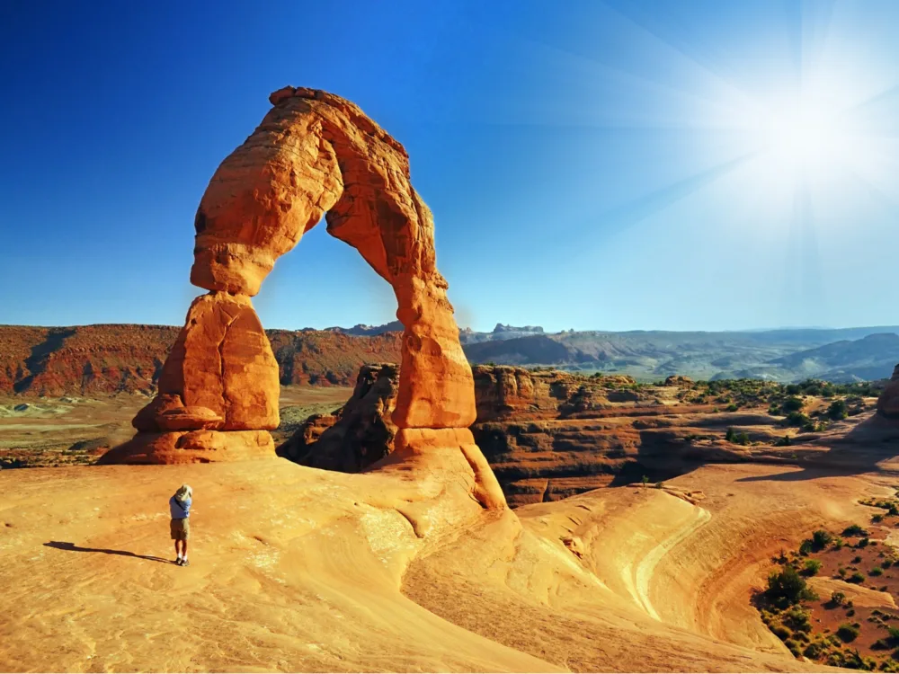 Famous Arches National (one of the best places to visit in Utah) Park with a guy standing next to a rock arch