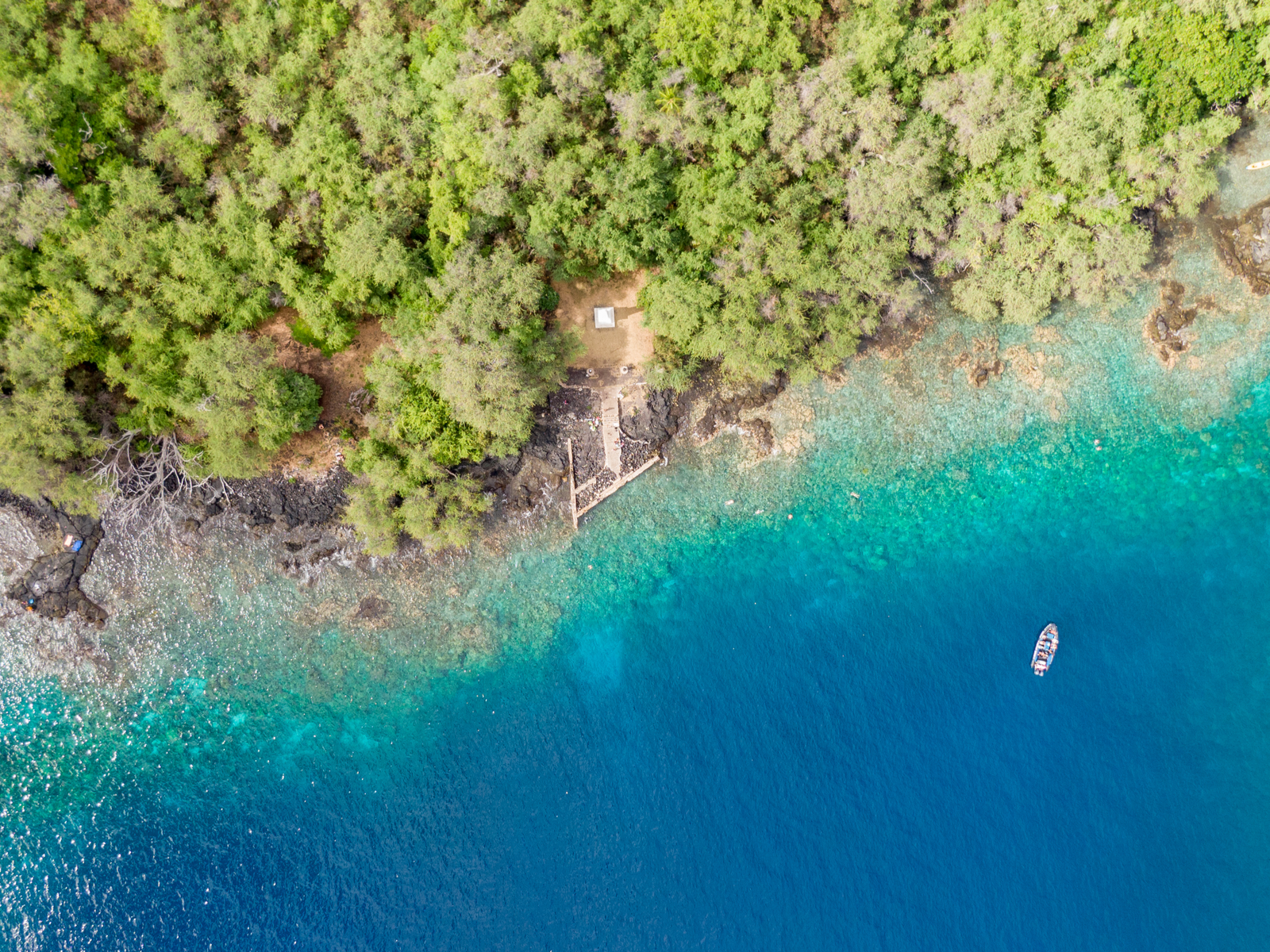 Overhead view of the stunning clear waters of Kealakekua Bay which makes it one of the best snorkeling spots in Hawaii, and of a small boat floating on the deeper waters