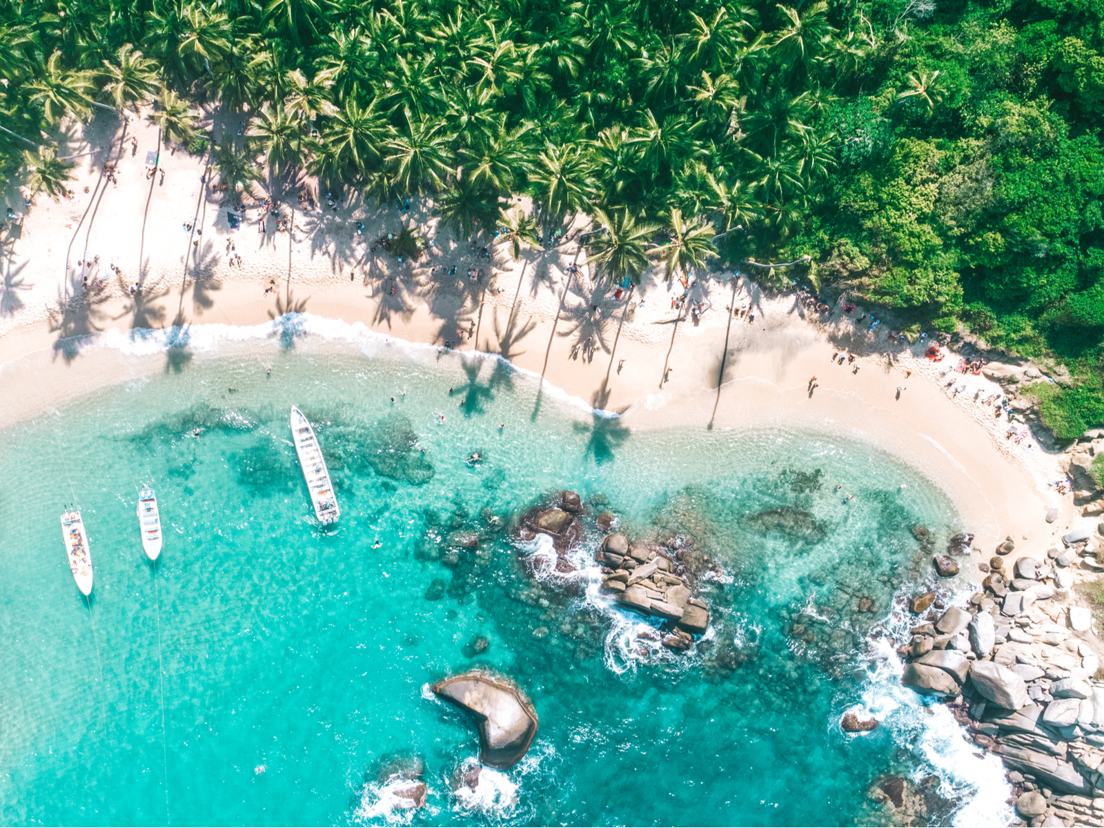 Tayrona National Park pictured in an aerial shot with boats next to the beach on teal water during the best time to visit Colombia