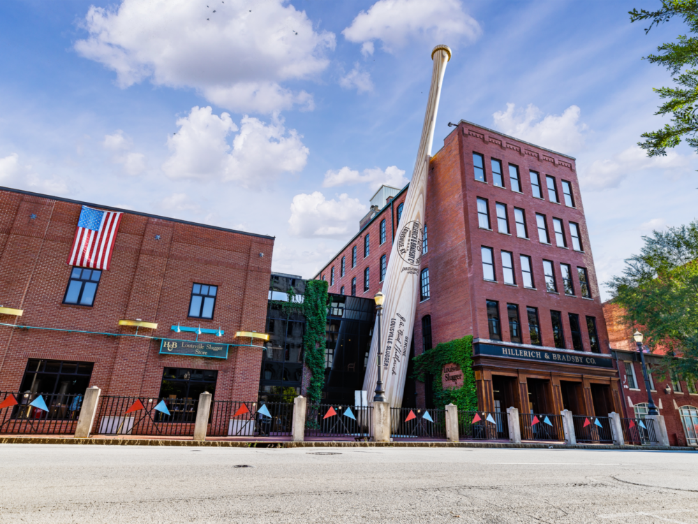 The iconic giant baseball bat leaning towards the Louisville Slugger Museum & Factory building, pictured in a worm's-eye view from the opposite street as a piece on the best things to do in Kentucky