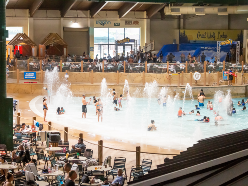 Some people in their swimwear enjoying the spouting waters in a shallow pool and some sitting on chairs outside pool perimeter in an indoor water park of Great Wolf Lodge, one of the best water parks in the USA