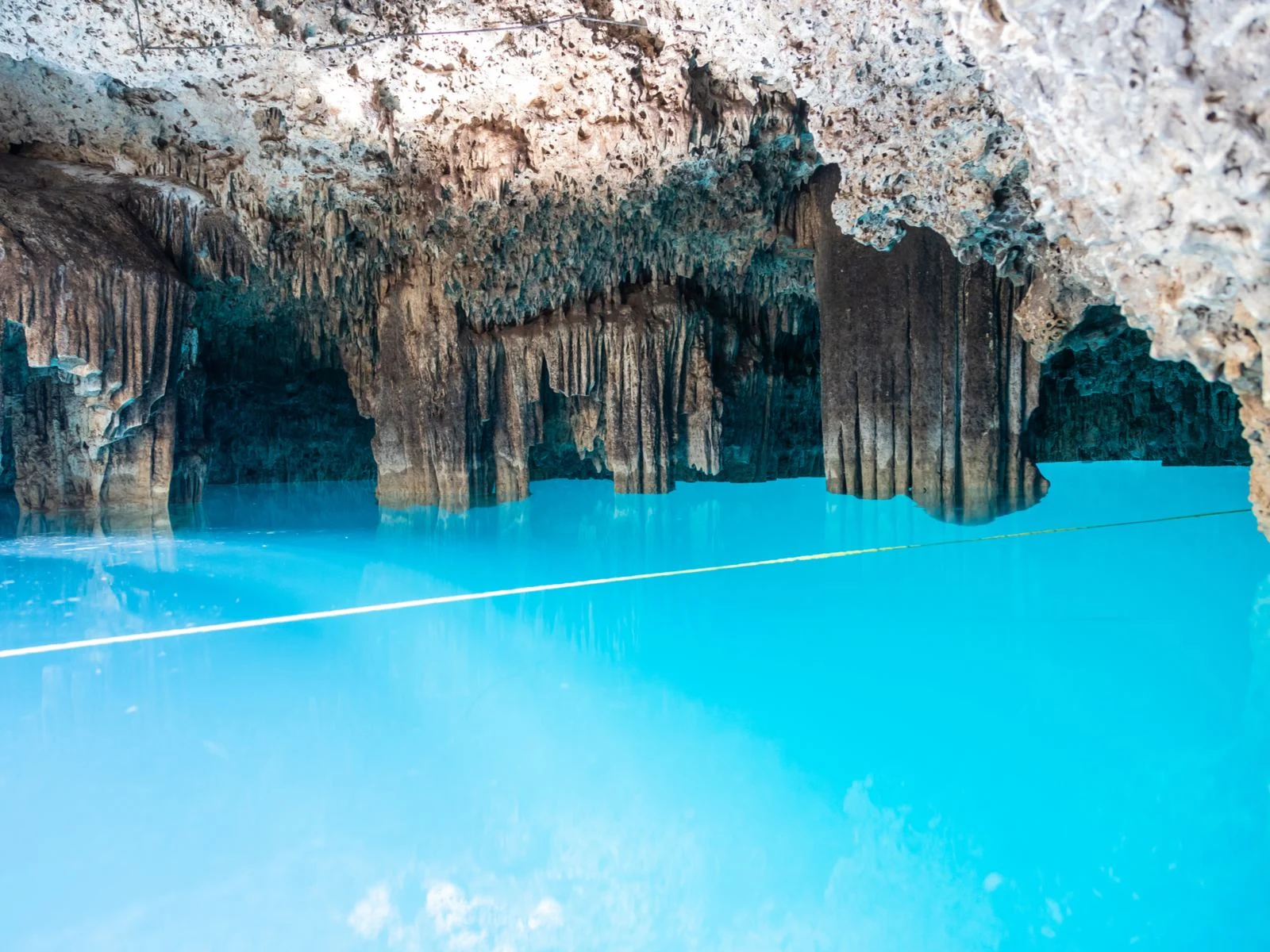 Cenote Siete Bocas, one of Mexico's best cenotes, pictured with neon blue water below rocks