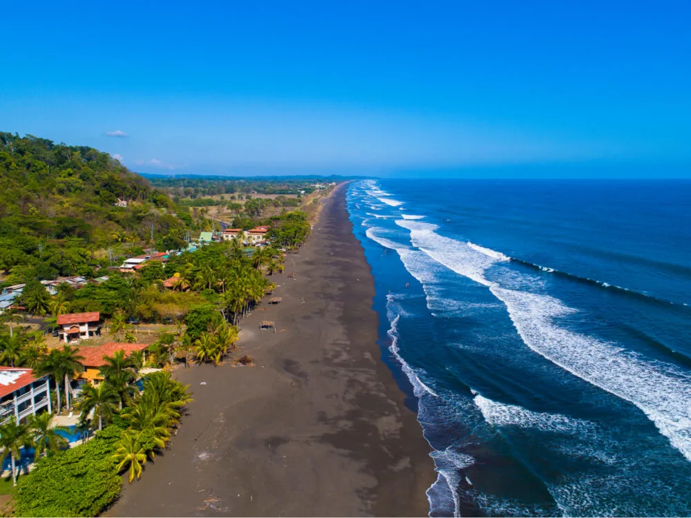 Aerial view on one of the best beaches in Costa Rica, Playa Hermosa with its dark fine sand, tall palm trees, and calm waves