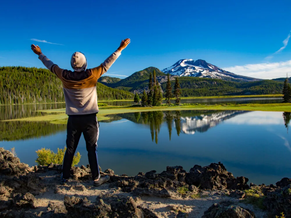Young man raising his arms over a lake with Mount Hood in the background of Bend, one of the best places to visit in Oregon