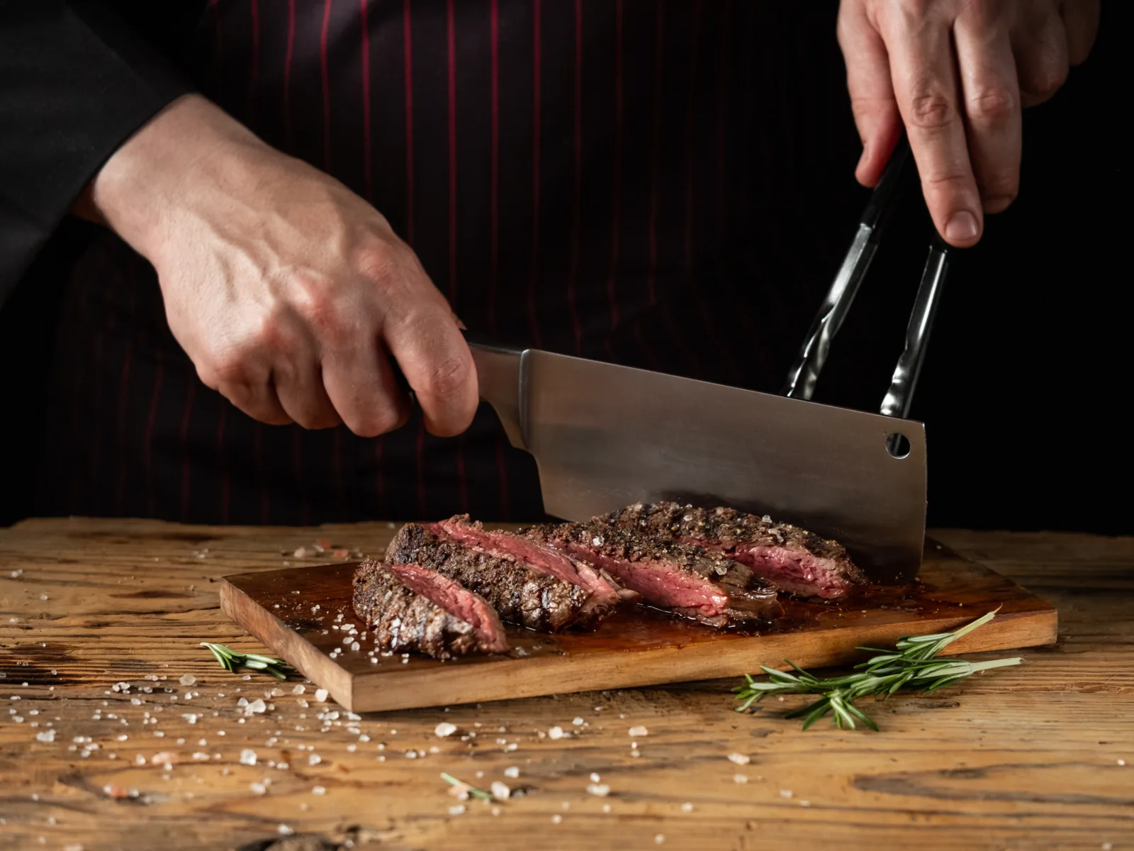 A chef cutting a salted steak on a wooden chopping board at Old Iceland Restaurant, one of the best restaurants in Iceland