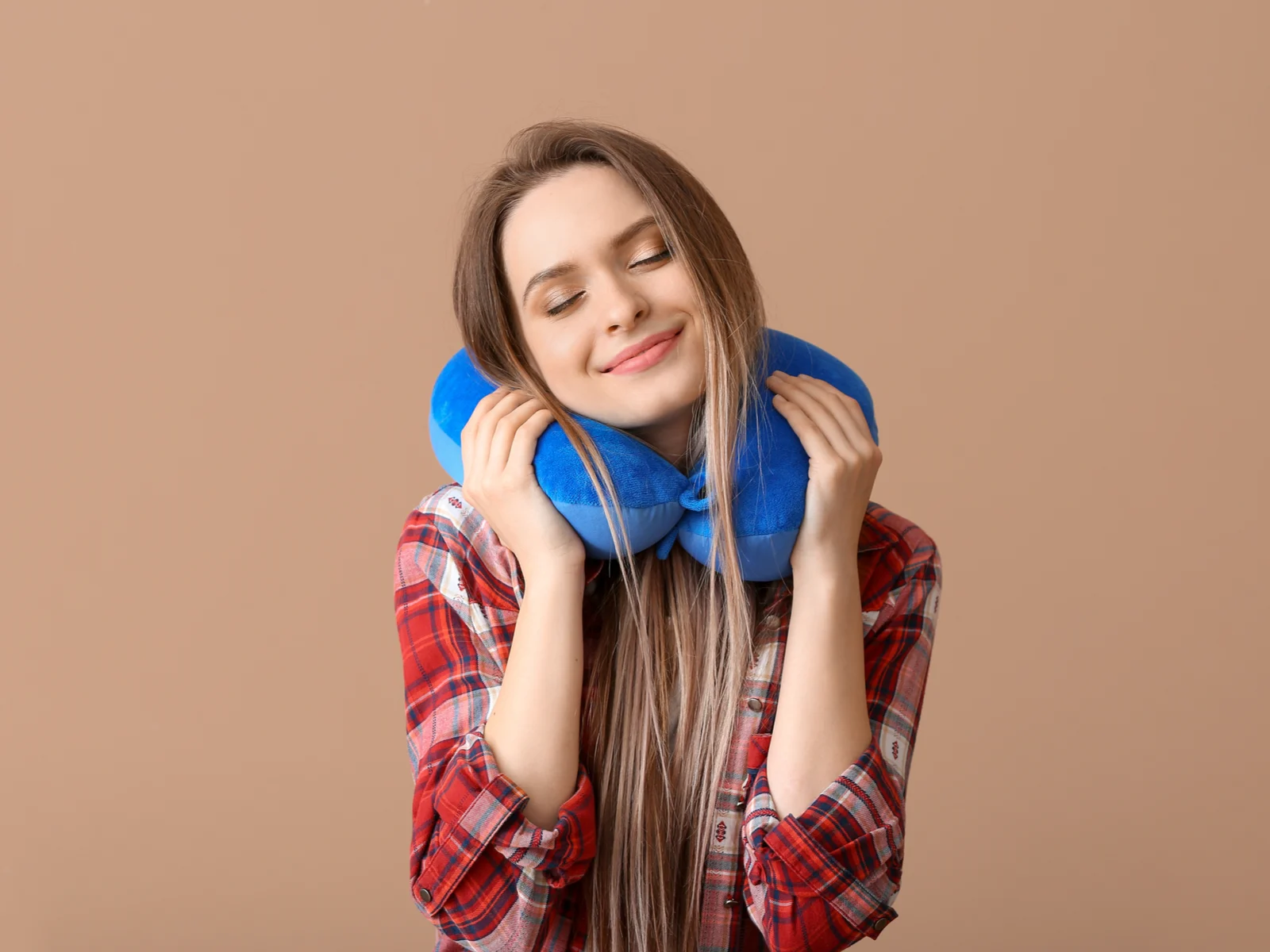 Young woman resting her head on the best travel pillow in a brown room
