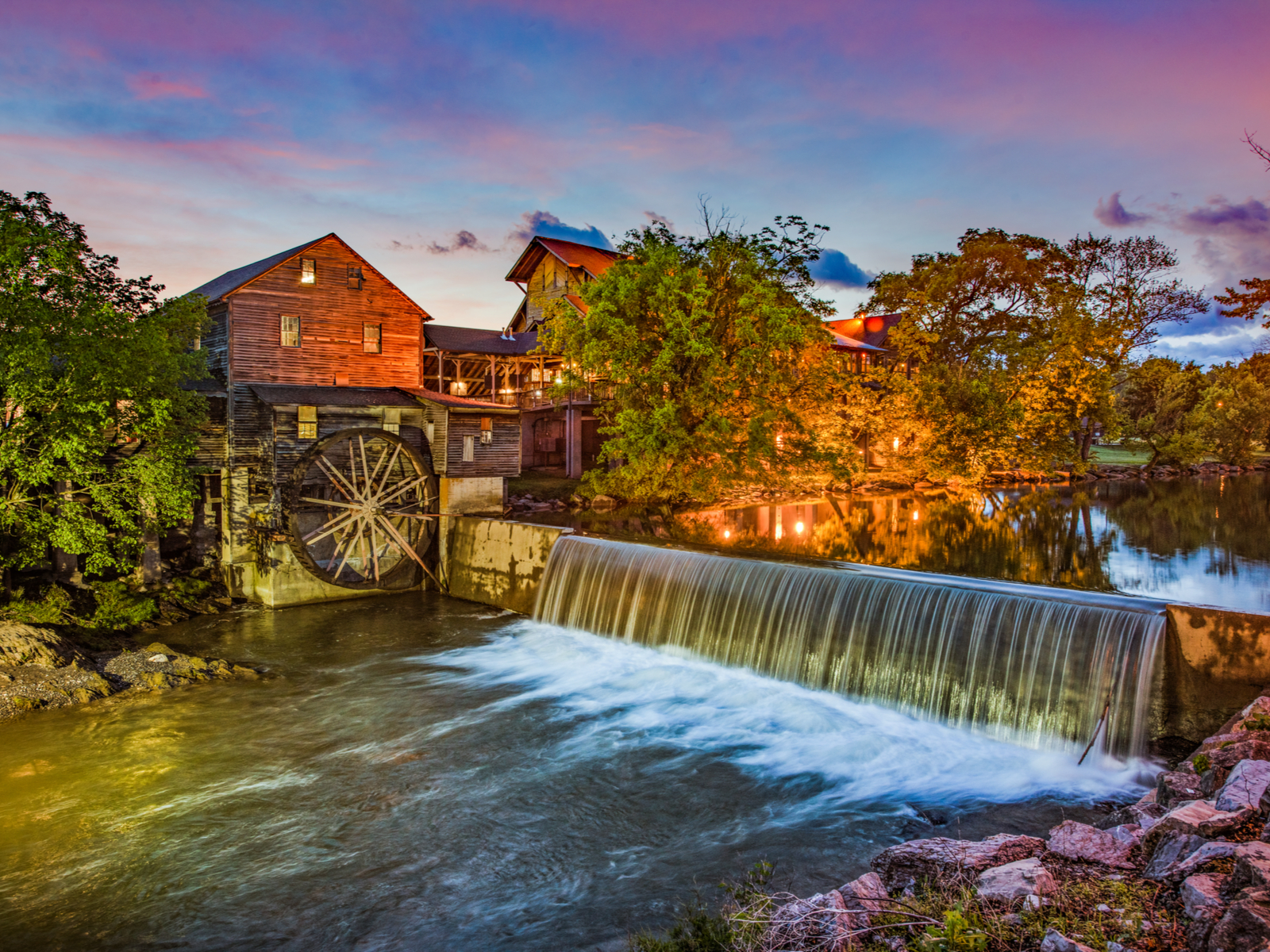 Evening view of the old mill in Pigeon Forge, one of the best things to do in Tennessee, with the river flowing over the dam