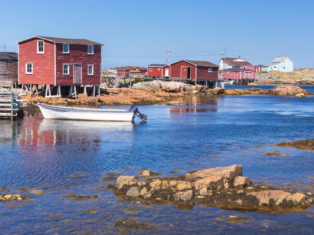 A docked small white boat and red colored fishing stages in a fishing village at Fogo Island, Newfoundland and Labrador, one of the best places to visit in Canada
