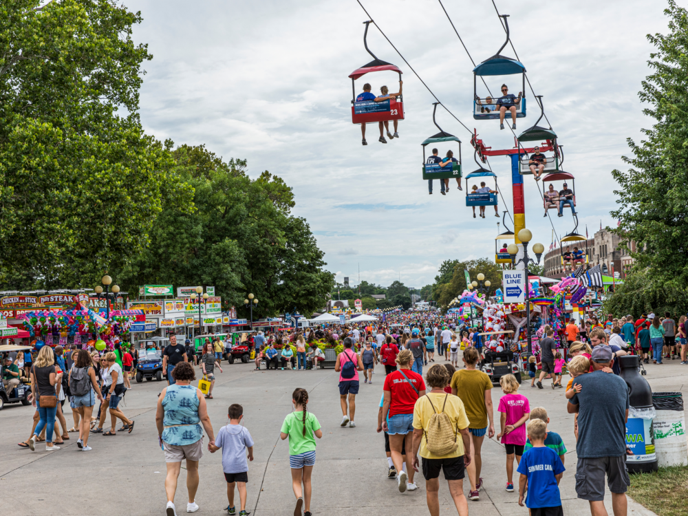 An exciting day at Iowa State Fair where locals and tourists enjoy various lively stalls and attractions, and some are taking a ride at chair lifts, a piece on what to see in Iowa