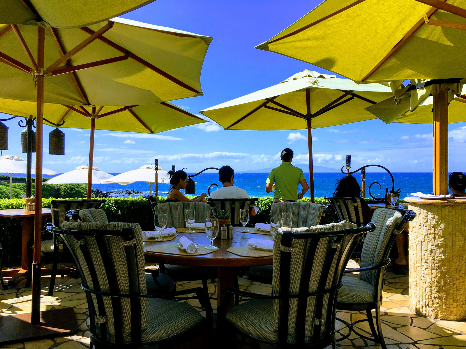 Visitors having a lovely lunch in a tropical beach under yellow patio umbrellas at one of the best restaurants in Kona, Hawaii